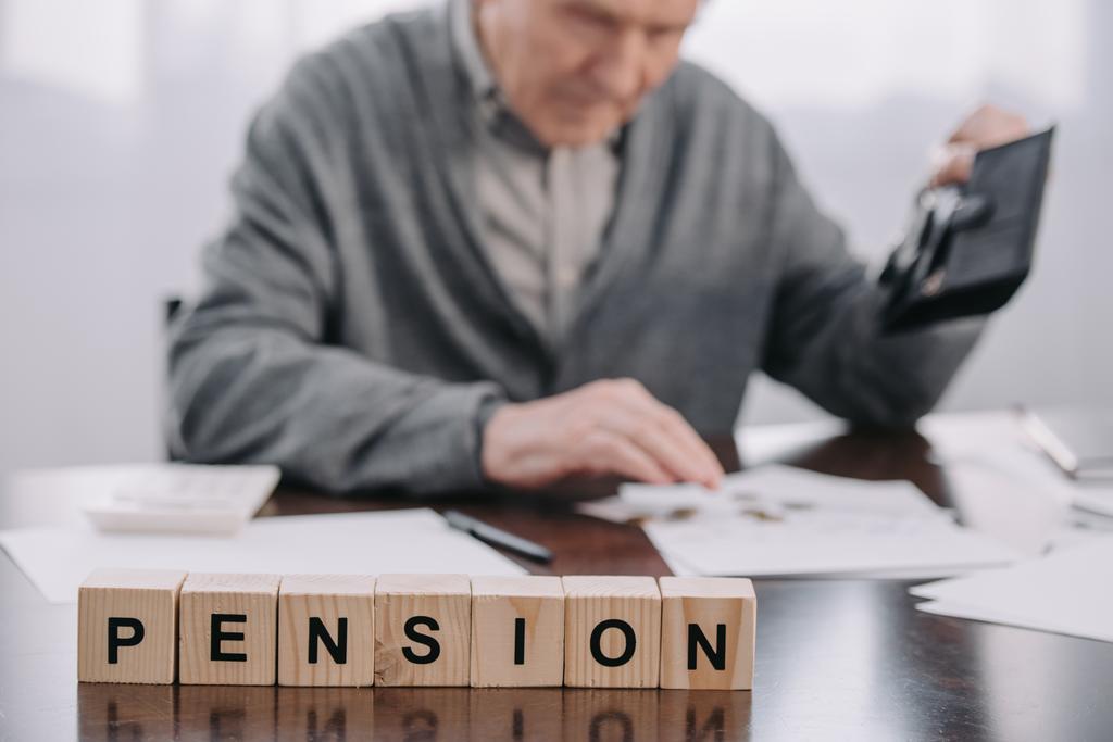 Selektiver Fokus des Wortes "Rente" aus Holzklötzen mit männlichem Rentner, der Geldbörse im Hintergrund hält - Foto, Bild