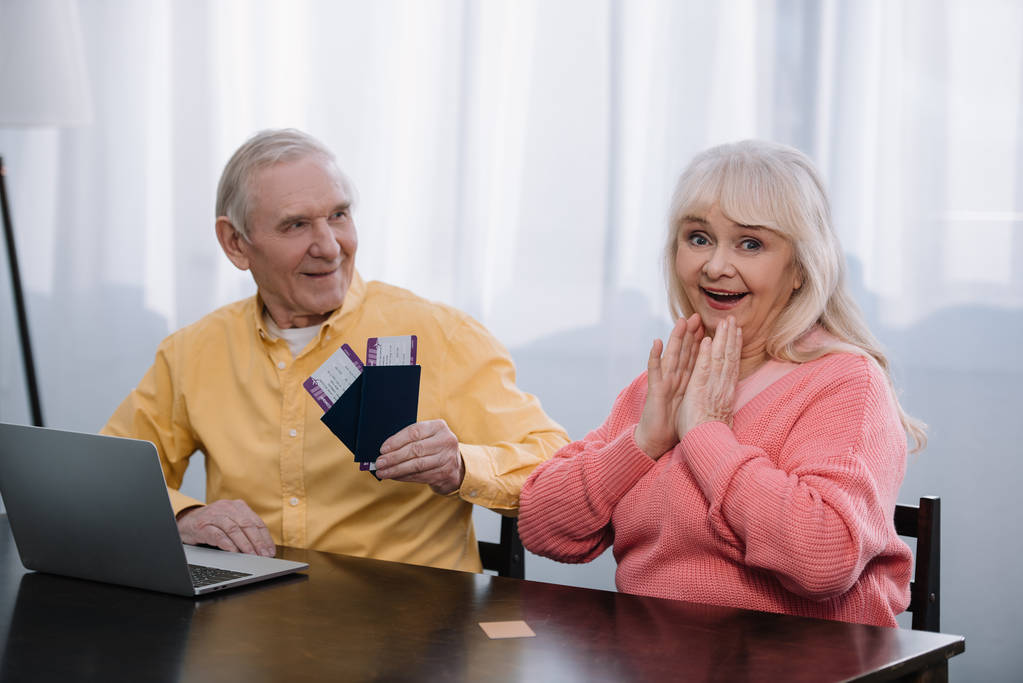 starszy człowiek posiadający bilety i paszporty w pobliżu zaskoczony Kobieta w domu  - Zdjęcie, obraz
