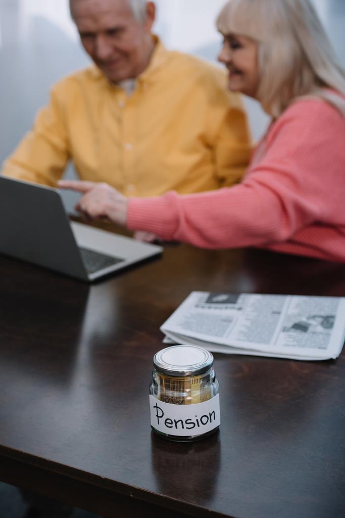 foyer sélectif de pot en verre avec lettrage "pension" et couple de personnes âgées à l'aide d'un ordinateur portable sur fond
 - Photo, image