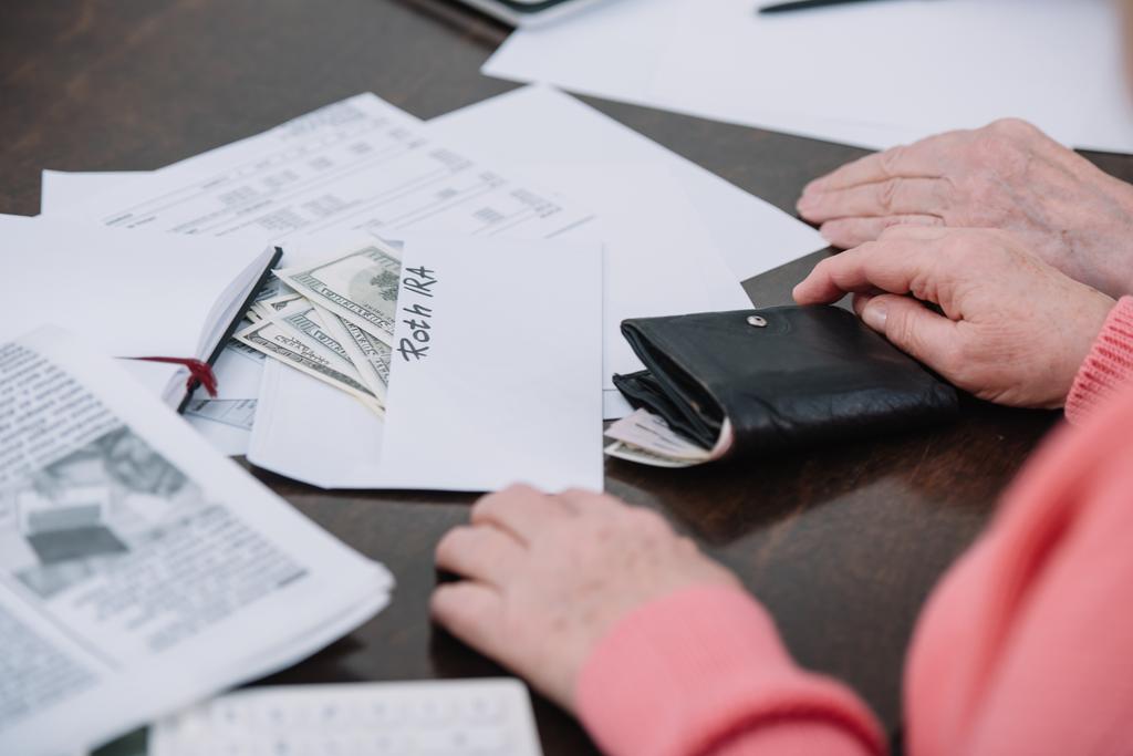 evrak, para ve zarf 'roth IRA' yazı ile masada oturan üst düzey çiftin kırpılmış görünümü  - Fotoğraf, Görsel