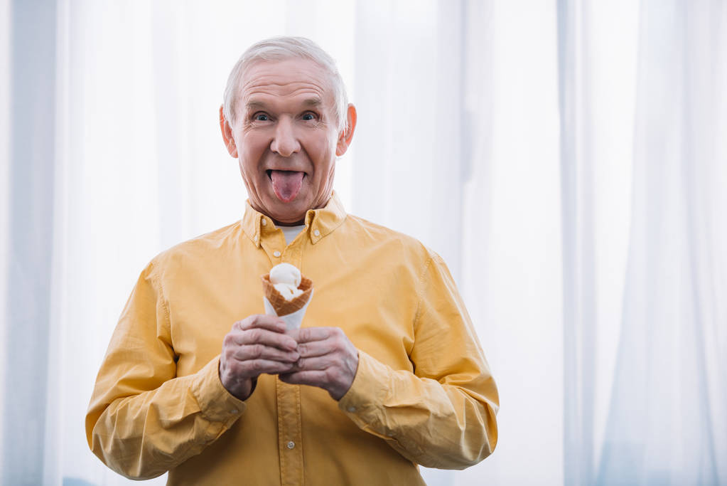 uomo anziano sporgente lingua, guardando la fotocamera e tenendo cono gelato a casa con spazio copia
 - Foto, immagini