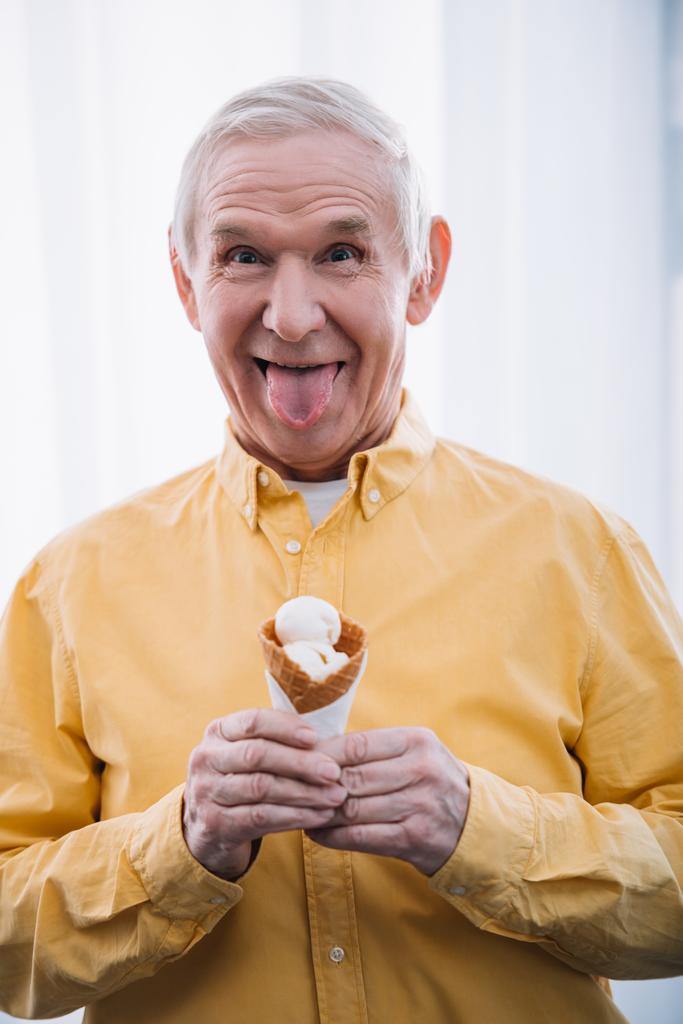 年配の男性のうち、家庭でアイス クリーム コーンを押しカメラ目線の舌を付着  - 写真・画像