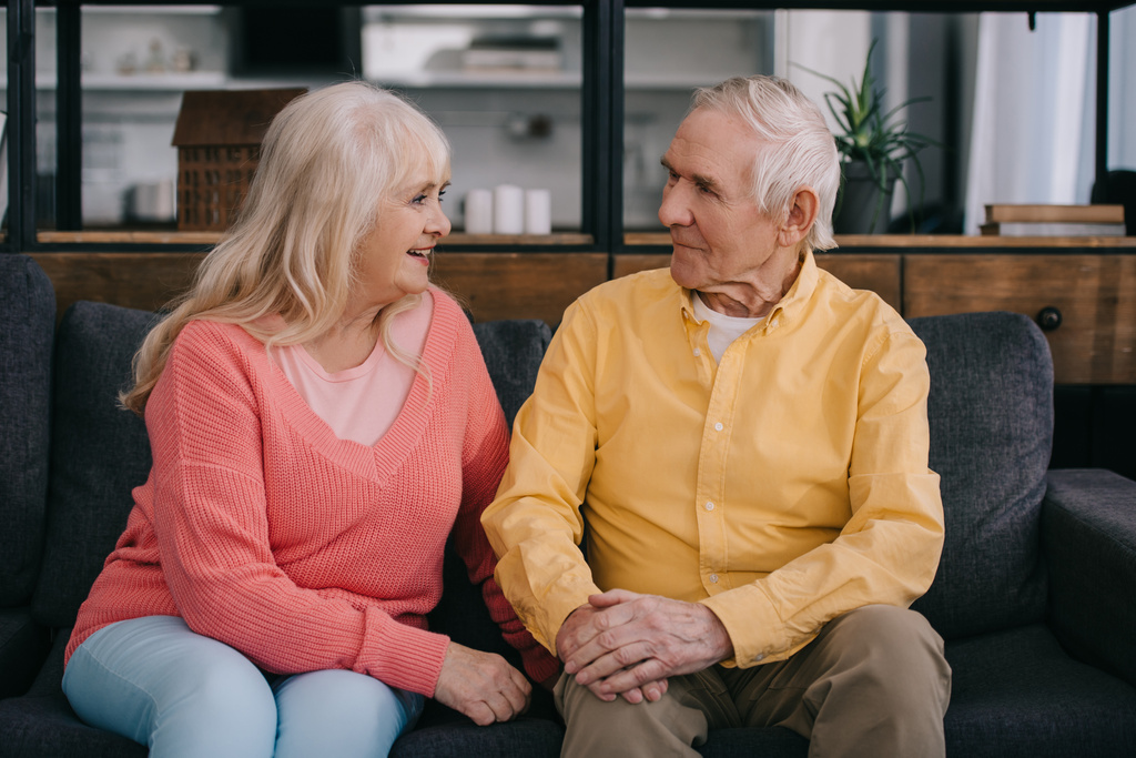 Seniorenpaar in legerer Kleidung sitzt auf Couch und schaut sich im Wohnzimmer an - Foto, Bild