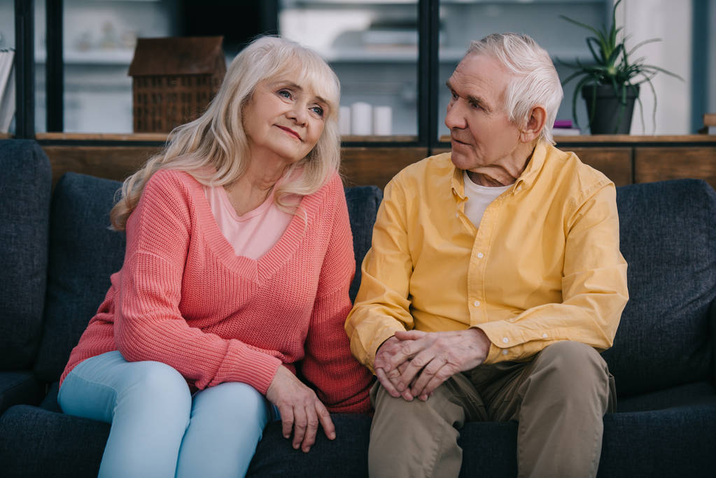 Oudere echtpaar in casual kleding zittend op de bank in de woonkamer - Foto, afbeelding