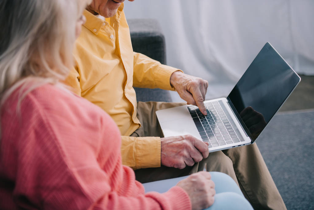 обрізаний вид на старшу пару, що сидить і використовує ноутбук з порожнім екраном вдома
 - Фото, зображення