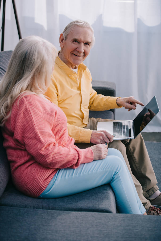 senior couple sitting on couch and using laptop at home - Photo, Image