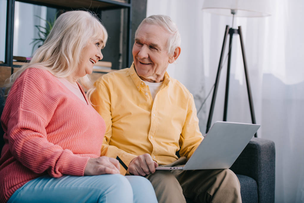 gülümseyen kıdemli çift evde online alışveriş yaparken laptop ve kredi kartı ile kanepede oturan - Fotoğraf, Görsel