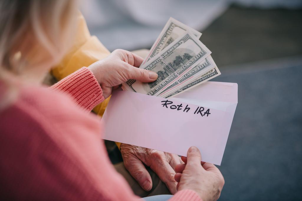 cropped view of senior couple holding envelope with 'roth ira' lettering and dollar banknotes - Photo, Image