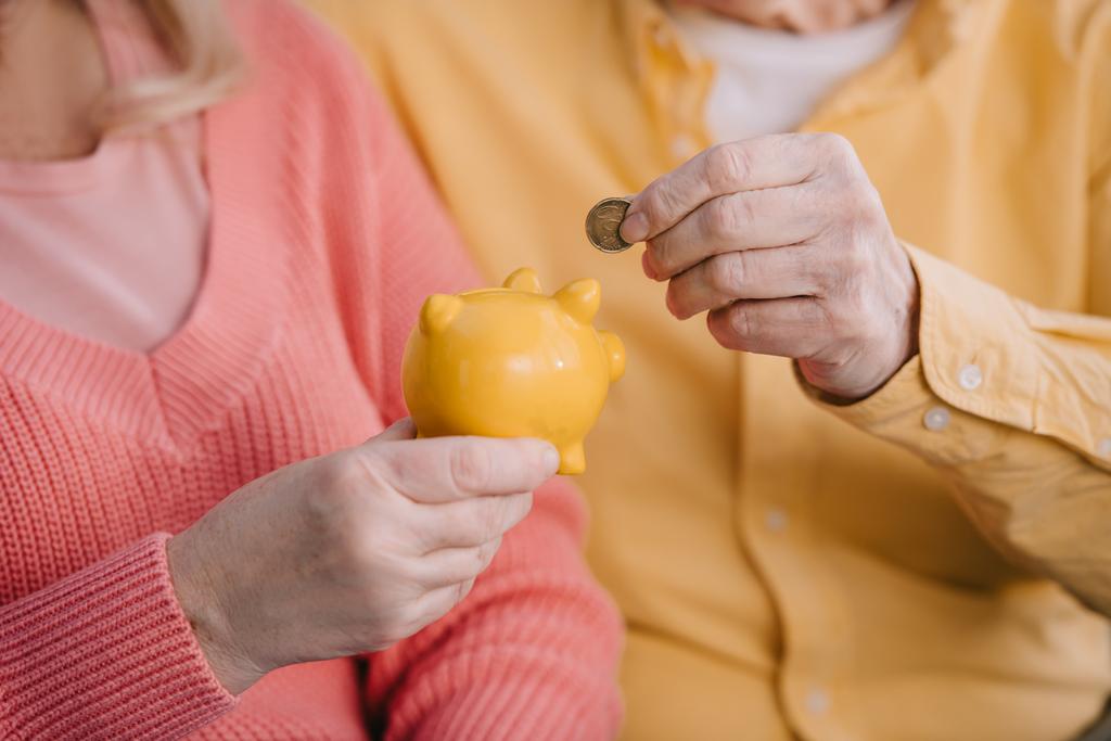 vista cortada do casal sênior colocando moeda no banco piggy amarelo
 - Foto, Imagem