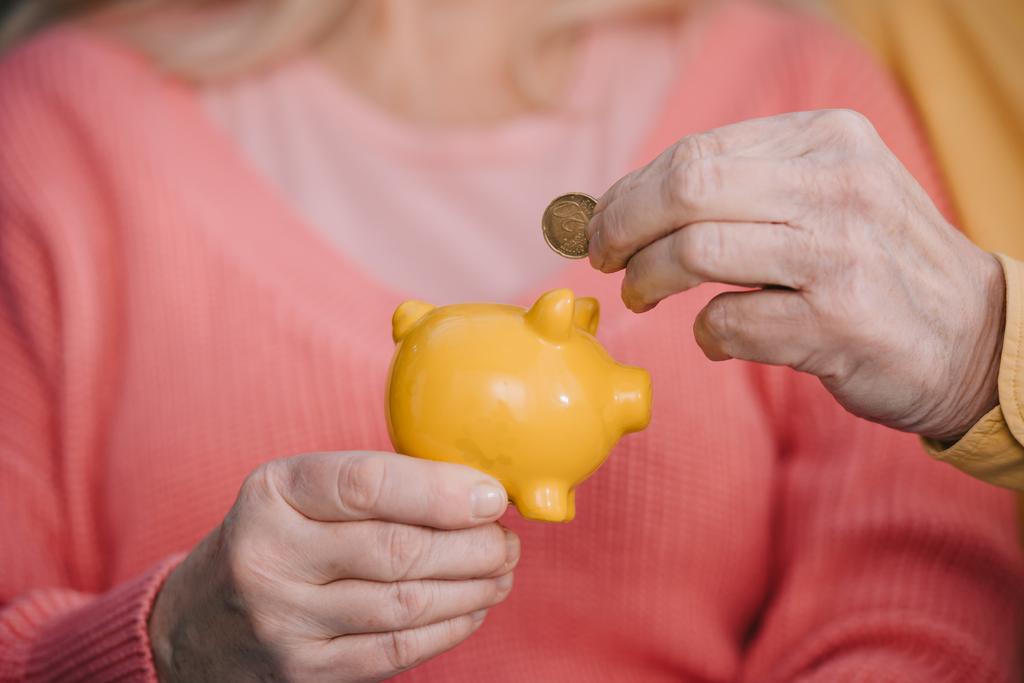 bijgesneden weergave van senior man munt aanbrengend gele piggy bank - Foto, afbeelding