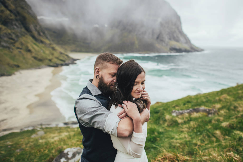 Ευτυχισμένος γάμος ταξιδιώτες ζευγάρι αγκαλιάζει το λόφο στην παραλία Kvalvika, Νορβηγία - Φωτογραφία, εικόνα
