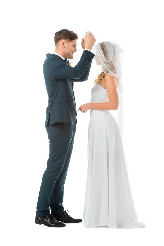 felice sposo sollevamento velo nuziale e guardando il viso spose isolato su bianco
 - Foto, immagini