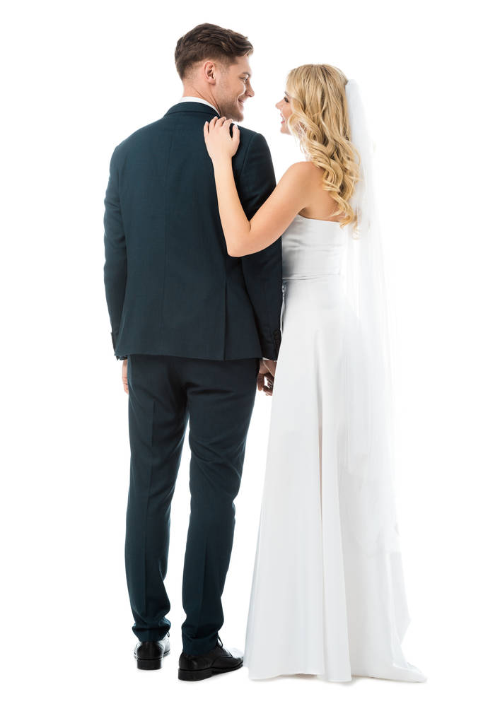 ευτυχισμένη νύφη στο λευκό νυφικό στέκεται κοντά χαμόγελο γαμπρός απομονωθεί σε λευκό - Φωτογραφία, εικόνα