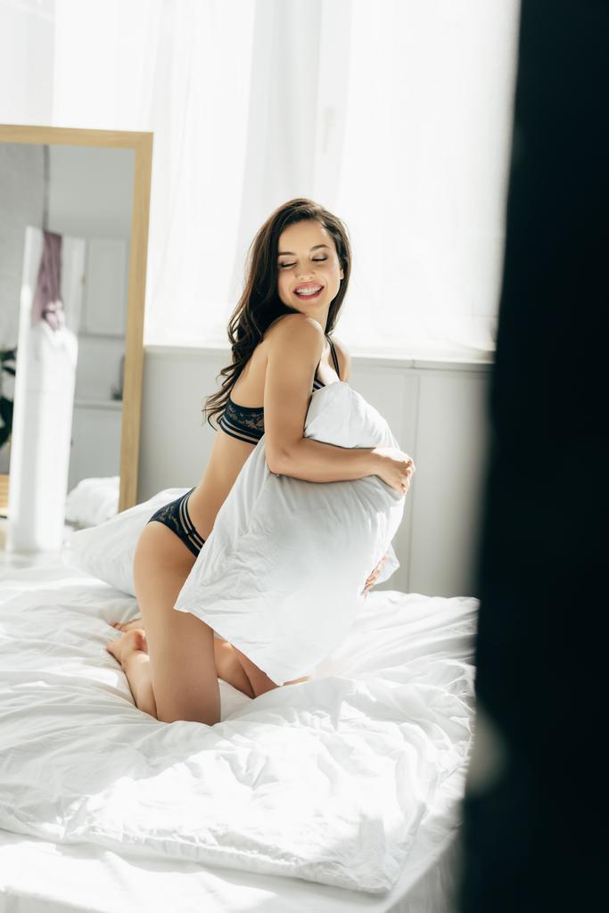 playful brunette woman in underwear holding pillow in hands - Photo, Image