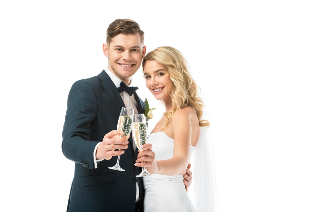 beautiful bride and handsome groom clinking glasses of champagne and looking at camera isolated on white - Photo, Image