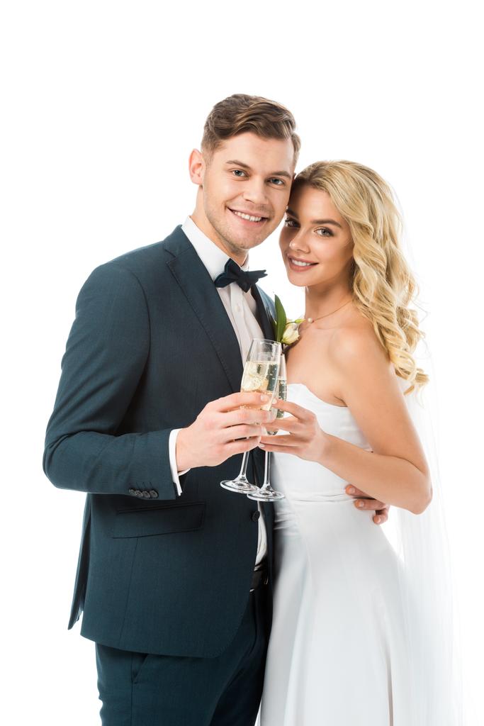 krásná nevěsta a pohledný ženich cinkání sklenic šampaňského a při pohledu na fotoaparát izolované na bílém - Fotografie, Obrázek
