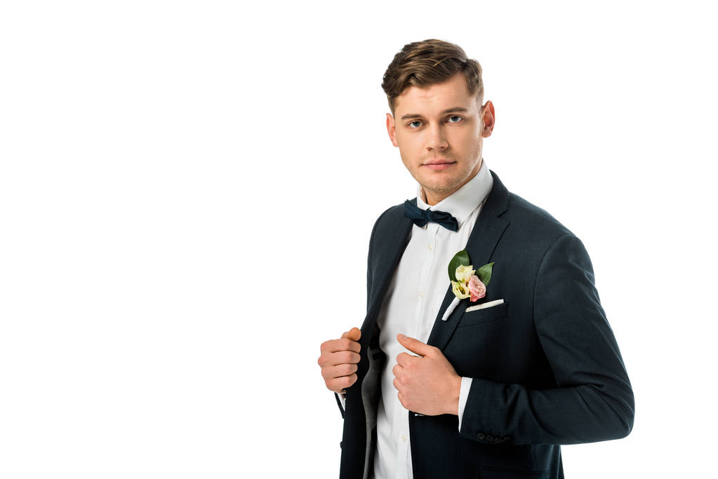 serious handsome bridegroom in bowtie and jacket with boutonniere looking at camera isolated on white - Photo, Image