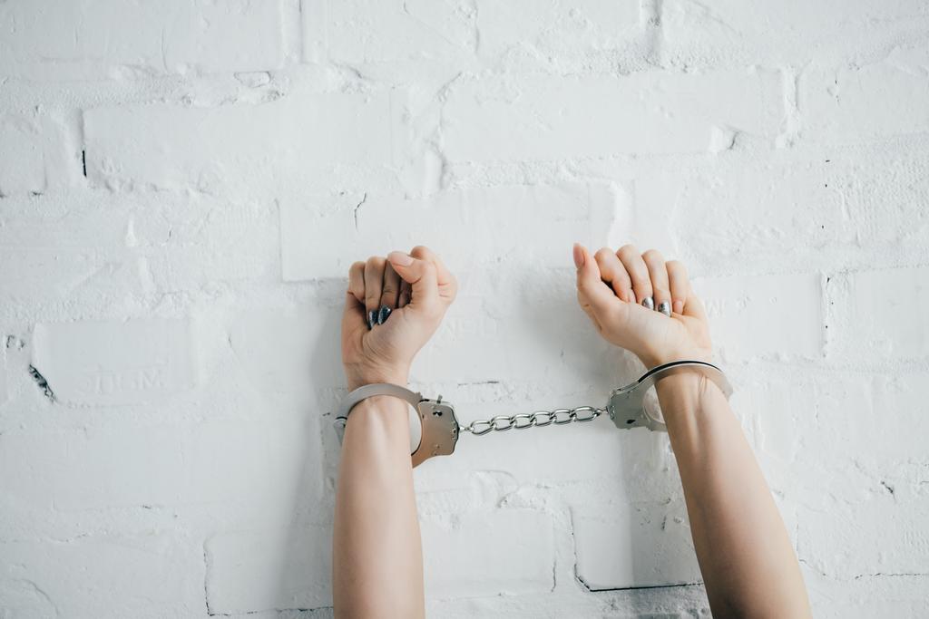 レンガの壁の近くの手錠をかけられ手で女性のトリミング ビュー - 写真・画像