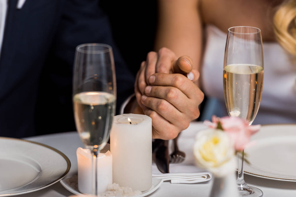 enfoque selectivo del hombre y la mujer tomados de la mano mientras están sentados en la mesa servida sobre fondo negro
 - Foto, Imagen