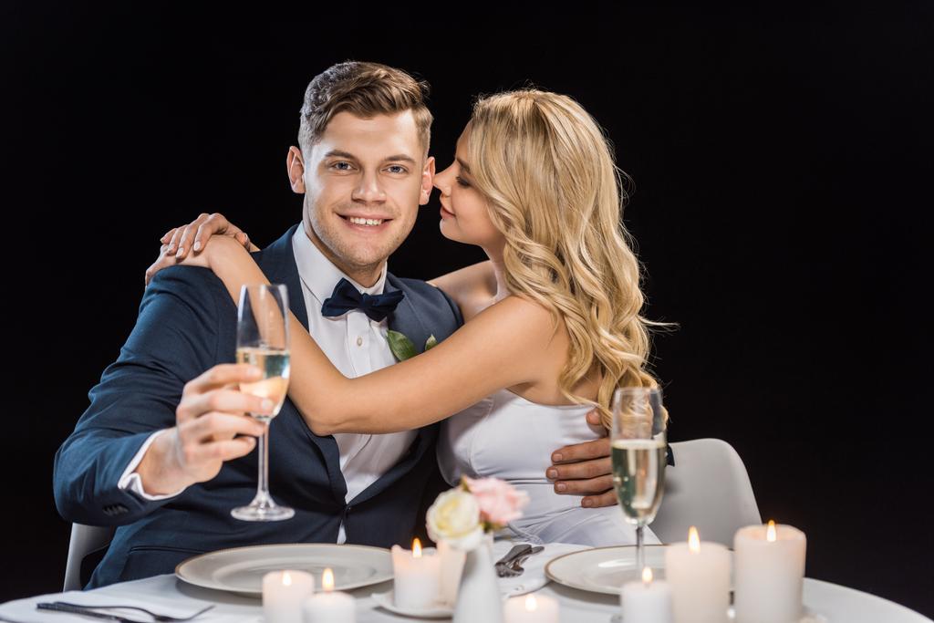 šťastná mladá nevěsta všeobjímající pohledný ženich se sklenkou šampaňského, samostatný na černém - Fotografie, Obrázek