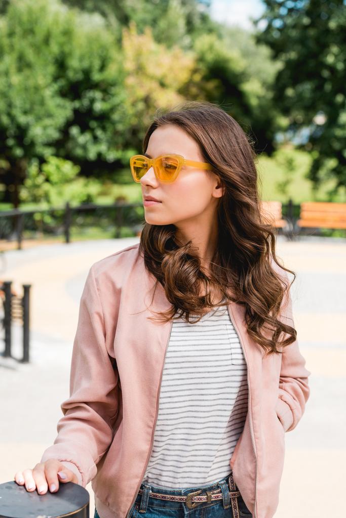 красивая девушка в солнечных очках, стоящая с рукой в кармане в парке
 - Фото, изображение