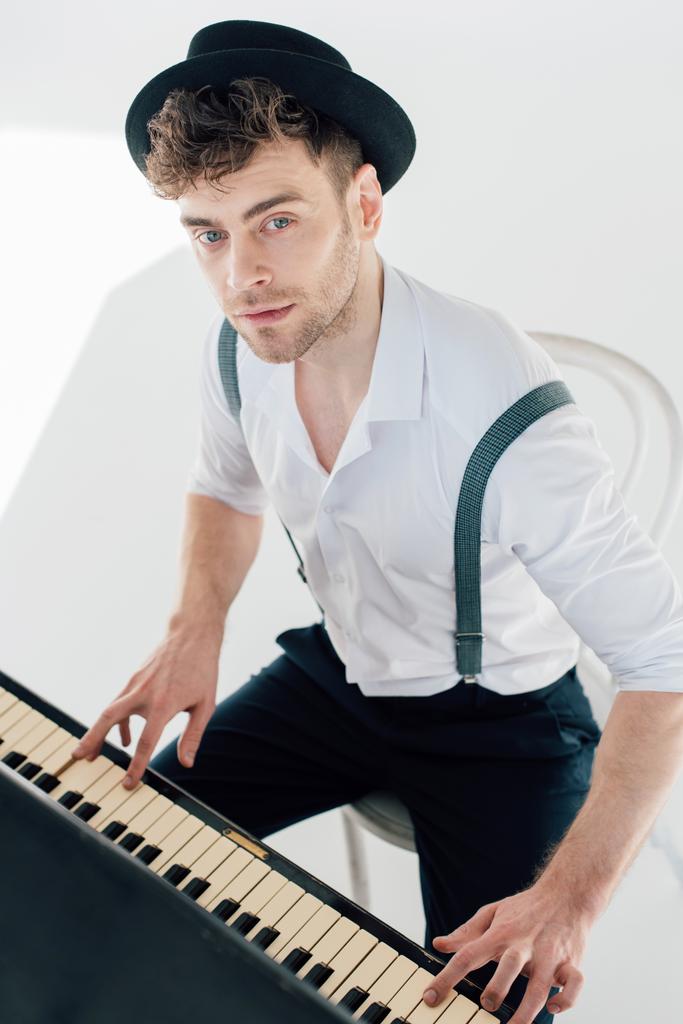 ονειρική πιανίστα σε άσπρο πουκάμισο και μαύρο καπέλο που παίζει πιάνο  - Φωτογραφία, εικόνα