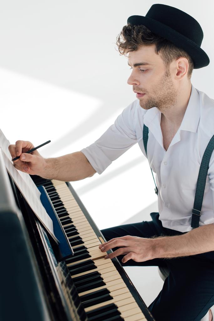 schöner Komponist schreibt in Notenbuch, während er am Klavier sitzt  - Foto, Bild