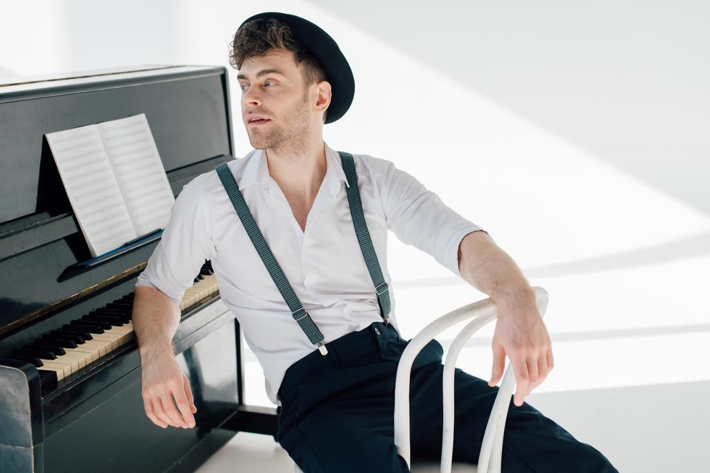 apuesto músico pensativo sentado en una silla blanca y apoyado en el piano
  - Foto, Imagen