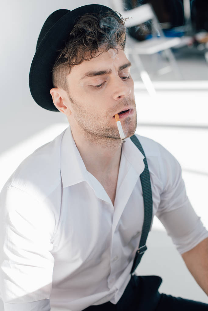 ernstige man in een wit overhemd en een zwarte hoed roken sigaret  - Foto, afbeelding