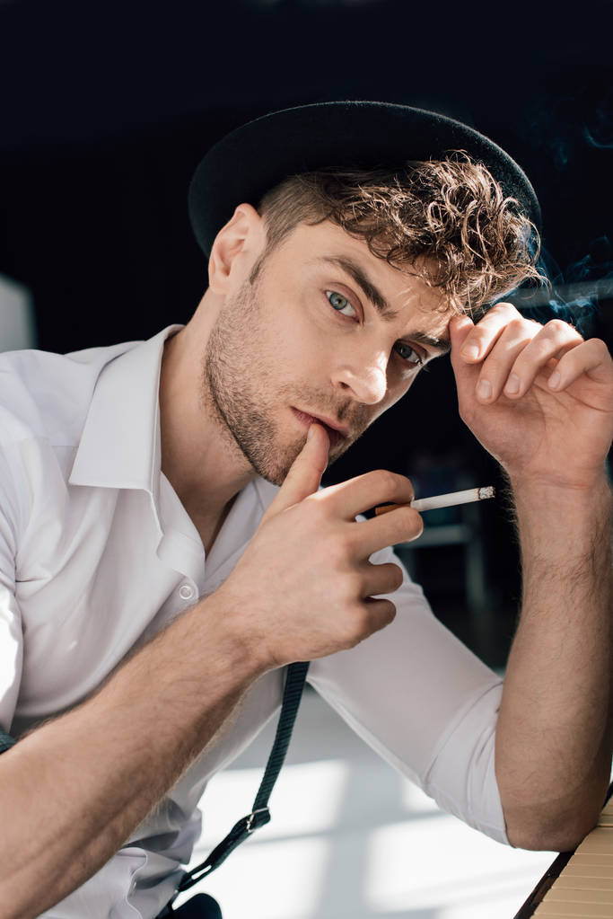 töprengő jóképű férfi, fehér inget és fekete kalap cigaretta a dohányzás - Fotó, kép
