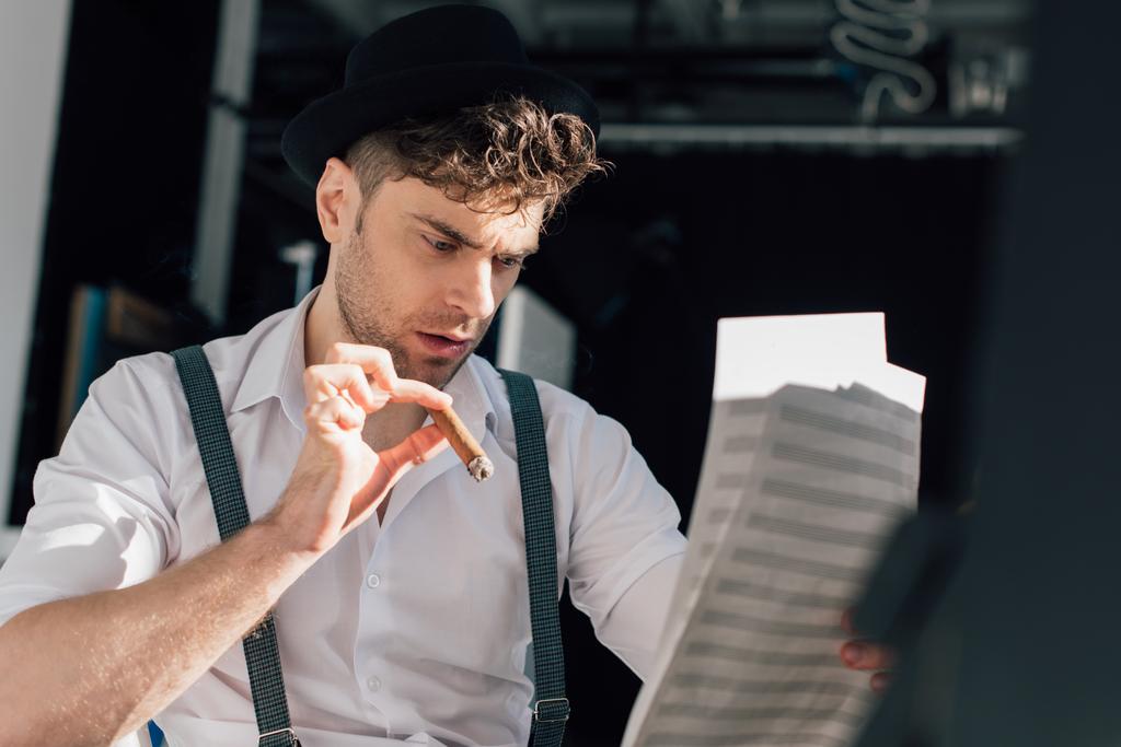 selektiver Fokus eines gutaussehenden Musikers mit Zigarre, Noten auf Notenblättern lesen  - Foto, Bild