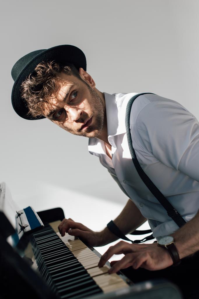 επιλεκτική εστίαση του σοβαρός μουσικός σε μαύρο καπέλο που παίζει πιάνο  - Φωτογραφία, εικόνα