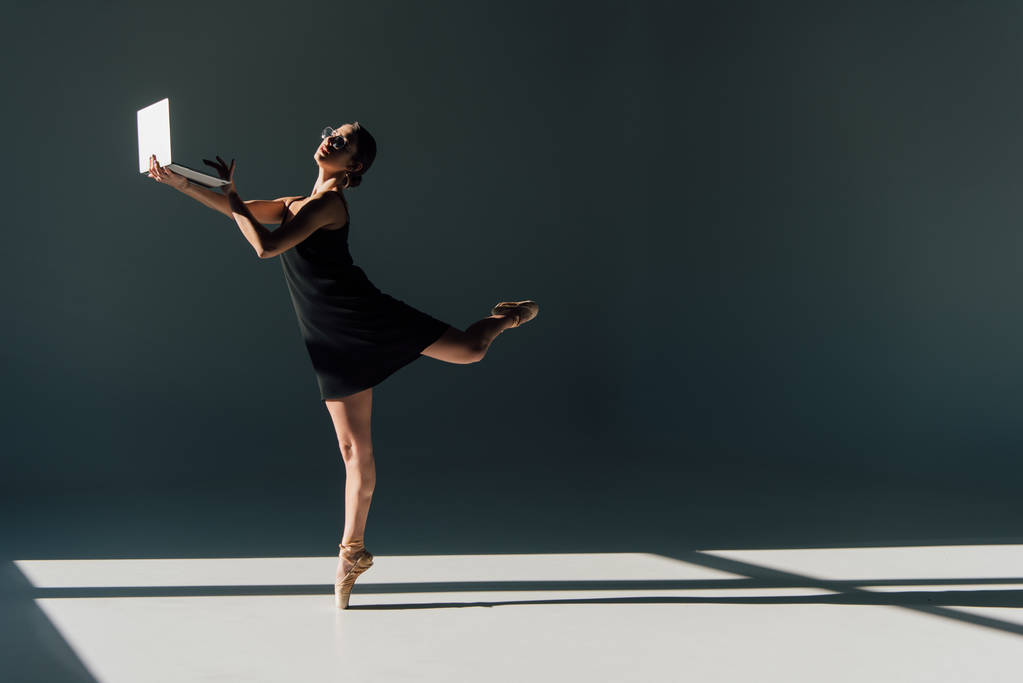 mladá baletka v černých šatech a brýle tančí s notebookem - Fotografie, Obrázek