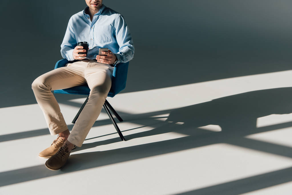 Kısmi smartphone ve kağıt Kupası sandalyede oturan adam görünümünü - Fotoğraf, Görsel