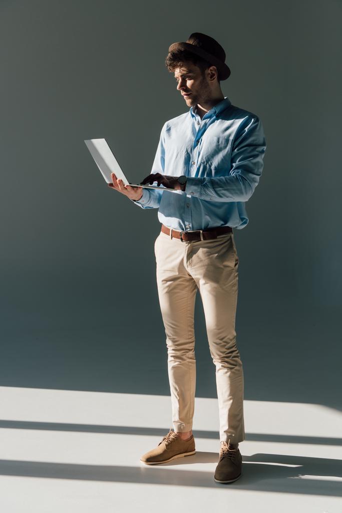 hombre guapo usando el ordenador portátil mientras está de pie en la luz del sol
  - Foto, imagen