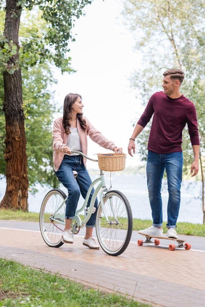 schöner Mann Longboard und Blick auf attraktive Freundin Fahrrad fahren  - Foto, Bild