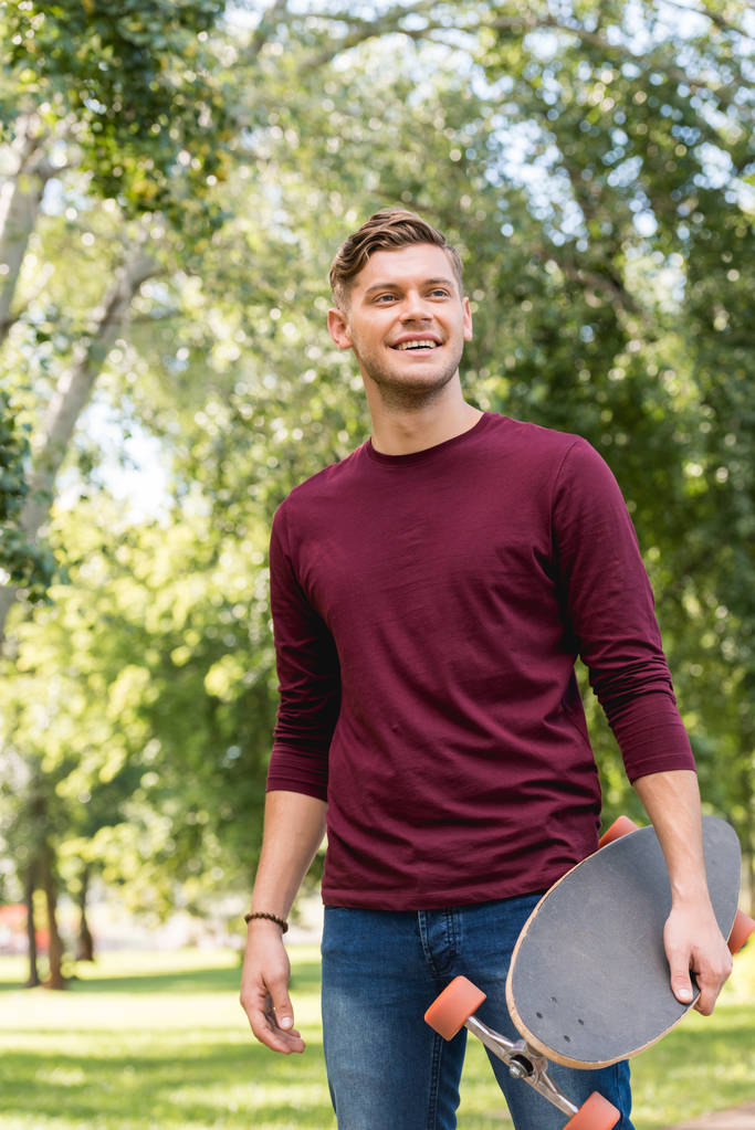 Красивый молодой человек улыбается, держа доску в парке
  - Фото, изображение