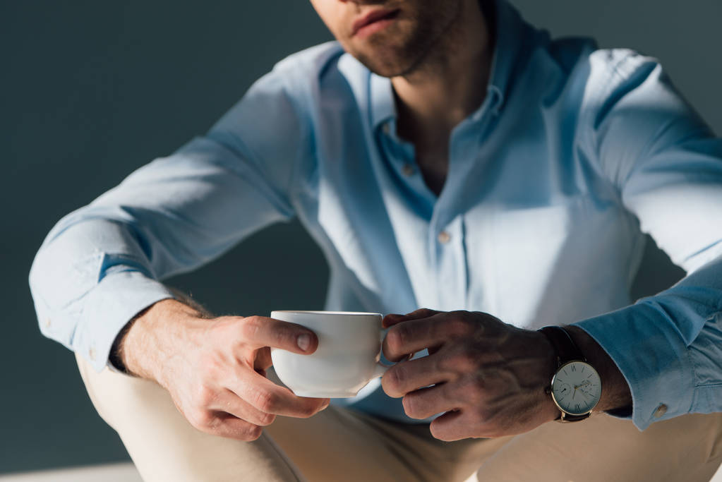 επιλεκτική εστίαση του κάθεται ο άνθρωπος κρατώντας φλιτζάνι καφέ  - Φωτογραφία, εικόνα