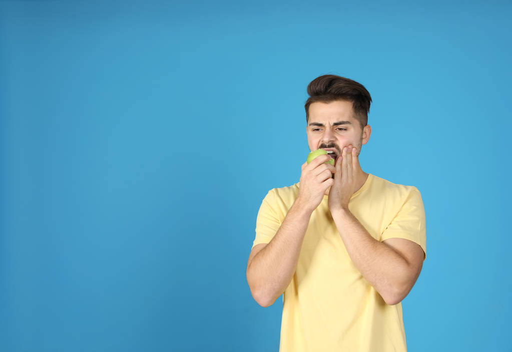 Giovane uomo emotivo con denti sensibili mangiare mela su sfondo di colore. Spazio per testo
 - Foto, immagini