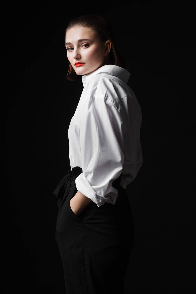 Retrato de una joven elegante con camisa blanca y pantalones negros. Interesante luz de estudio
 - Foto, imagen