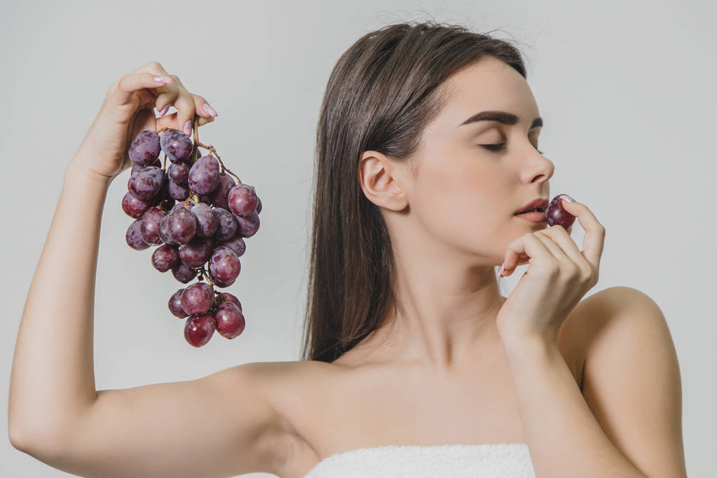 Beautiful young brunette girl with a happy smile. Holding a bunch of fresh grapes in hand, isolated on a white background. - Photo, Image
