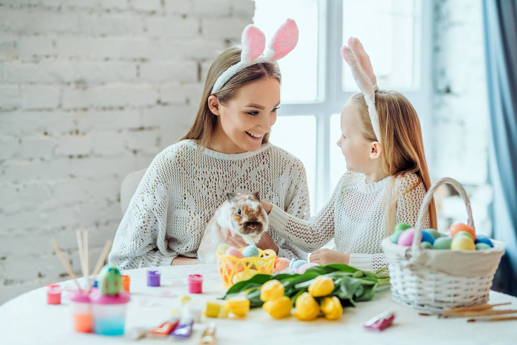 schau mal, was für ein niedliches Kaninchen. Die kleine Tochter streichelt mit ihrer Mutter ein häusliches Schmuckkaninchen. - Foto, Bild