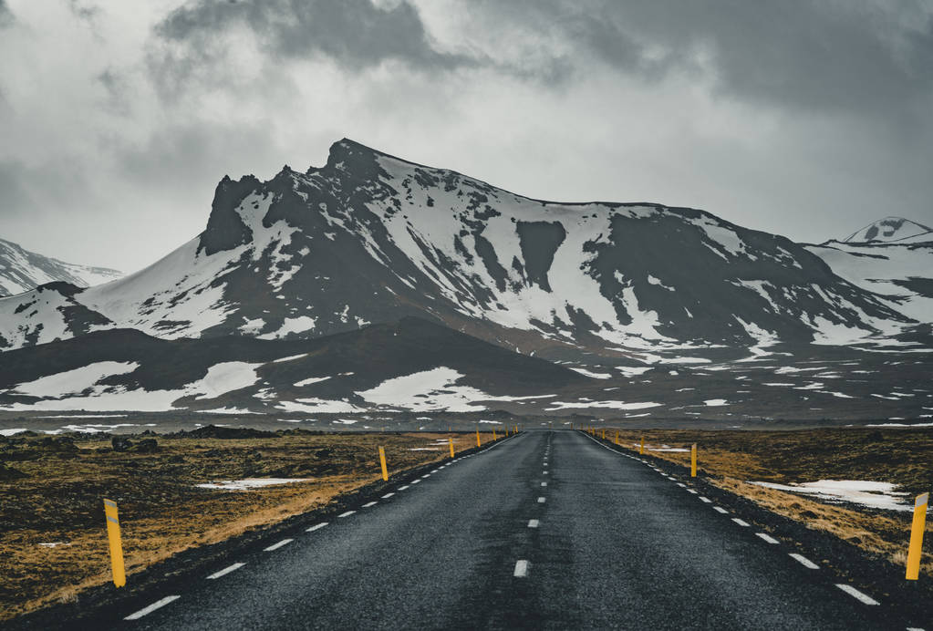 Perspectief van de kronkelende weg in IJsland met sneeuw bergketen achtergrond op bewolkte dag herfst seizoen IJsland. - Foto, afbeelding