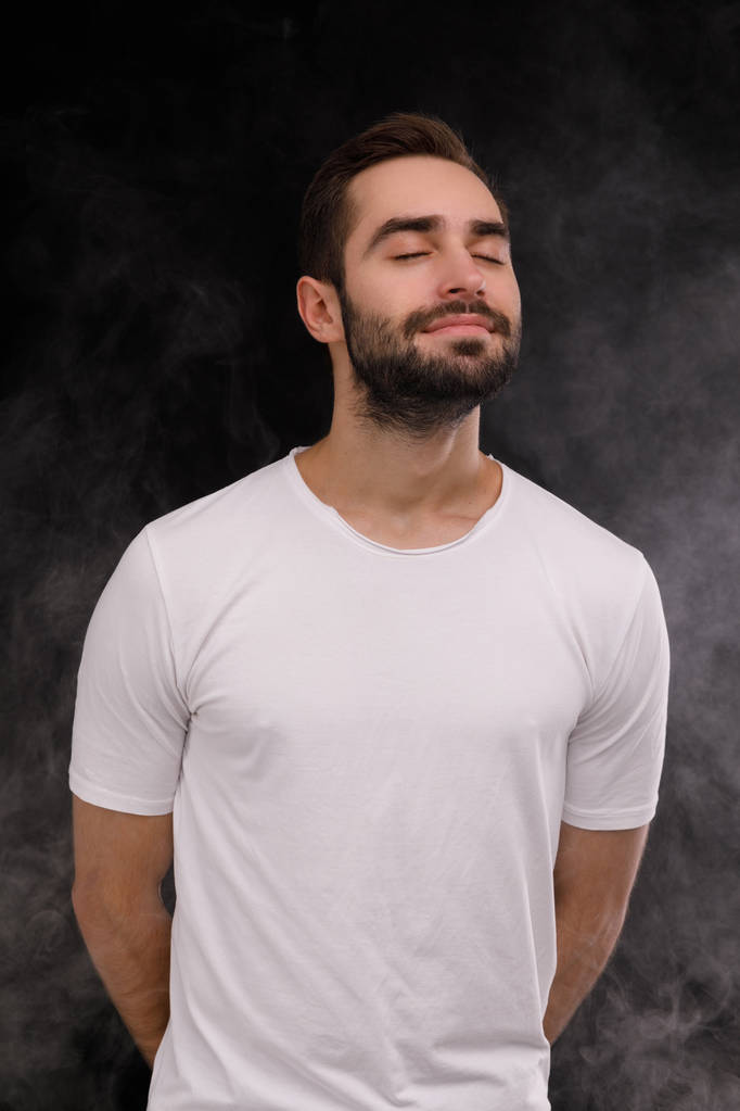 chico en camiseta blanca inhala humo sobre un fondo negro
 - Foto, imagen
