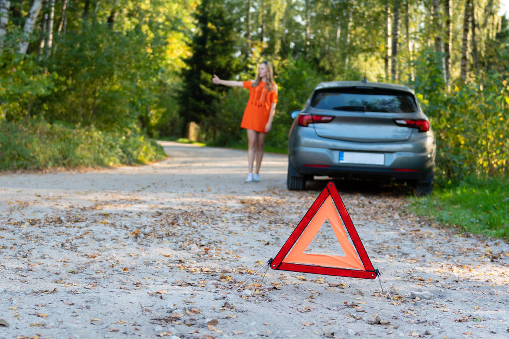 Stressaava nuori nainen kuljettaja liftaa ja pysäyttää autoja, pyytää apua kuin on ongelmia rikki auto, käyttää punainen kolmio merkki varoittaa kuljettajia stop. (valikoiva kohdentaminen
) - Valokuva, kuva