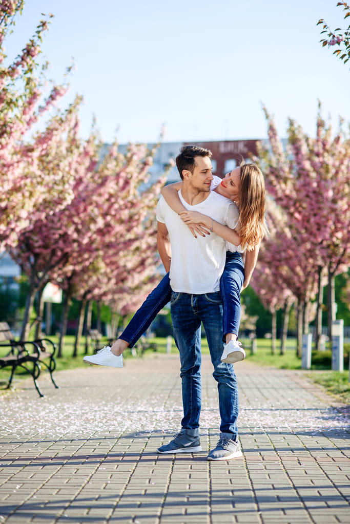 Έννοια πάθος και αγάπη. Άνδρας και γυναίκα φιλιά στον ανθισμένο κήπο την άνοιξη. Ζευγάρι αγκαλιές κοντά σε δέντρα sakura. Ερωτευμένο ζευγάρι περνούν χρόνο στον κήπο την άνοιξη. - Φωτογραφία, εικόνα