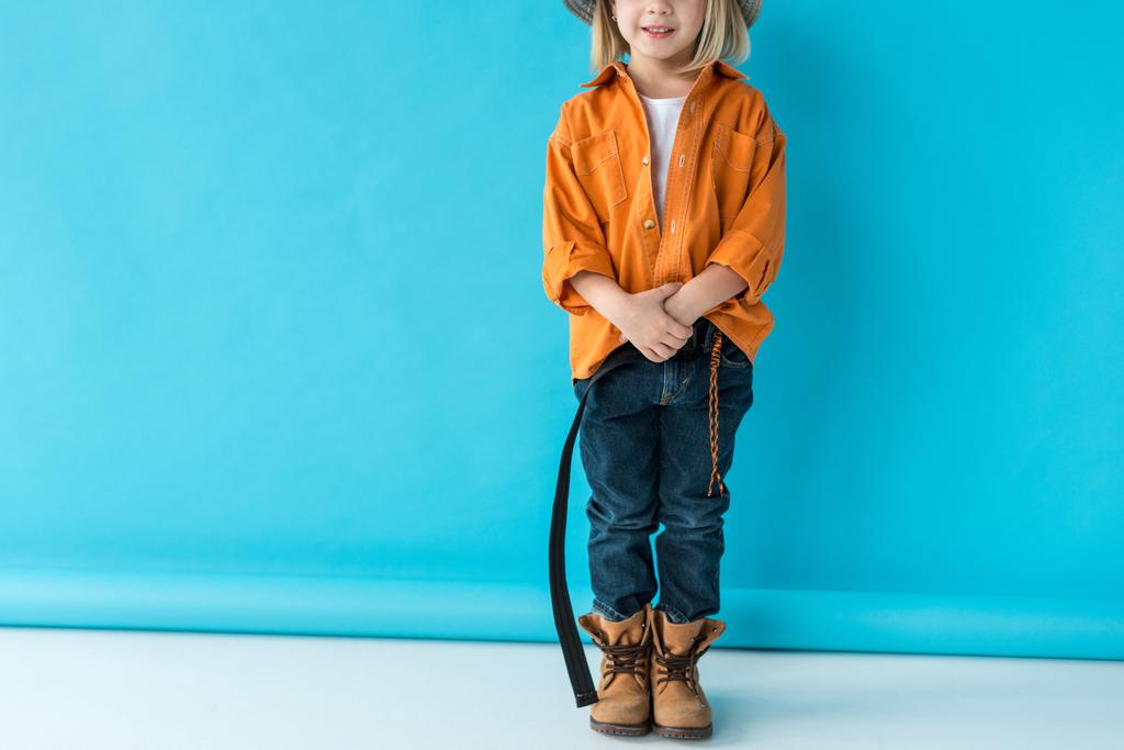обрізаний вид дитини в джинсах і помаранчевій сорочці на синьому фоні
  - Фото, зображення