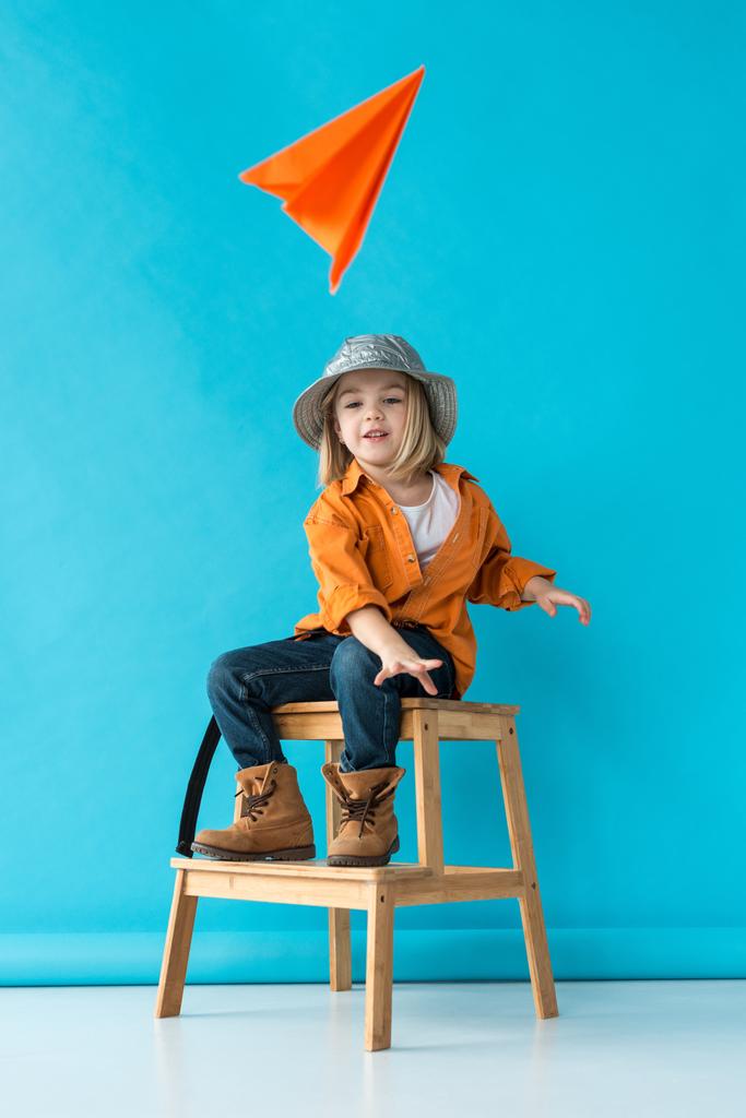 enfant en jeans et chemise orange assis sur les escaliers et jouer avec l'avion en papier
  - Photo, image