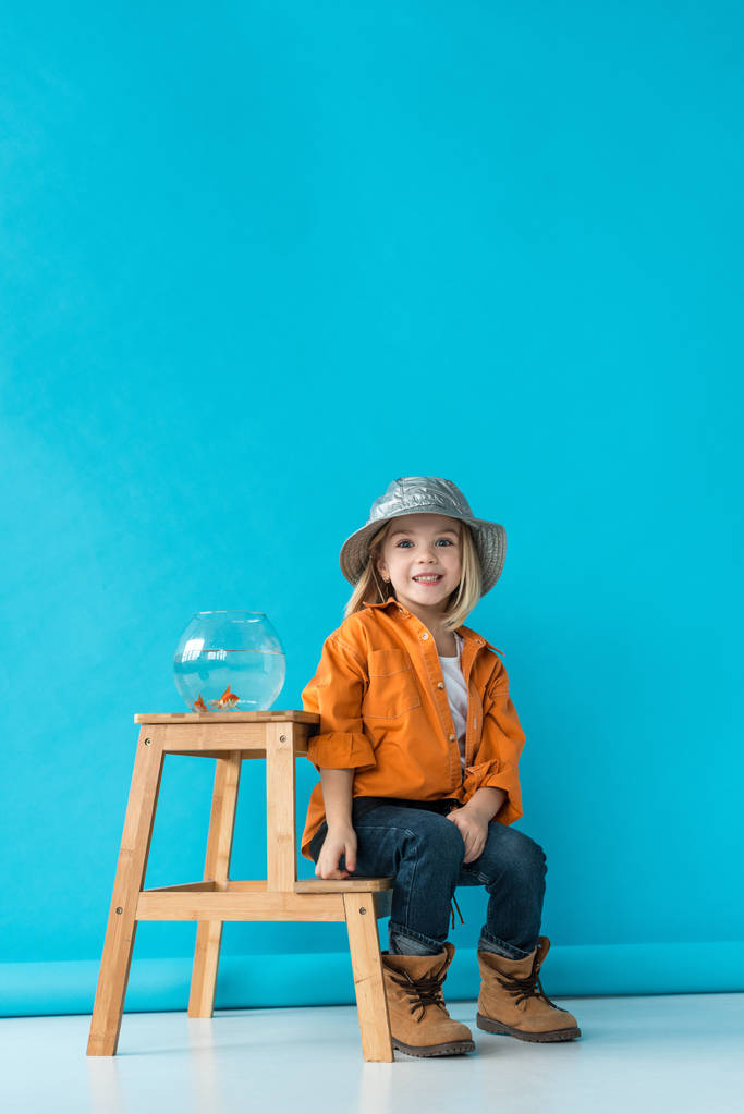 niño en jeans y camisa naranja sentado en las escaleras con pecera de vidrio
 - Foto, Imagen