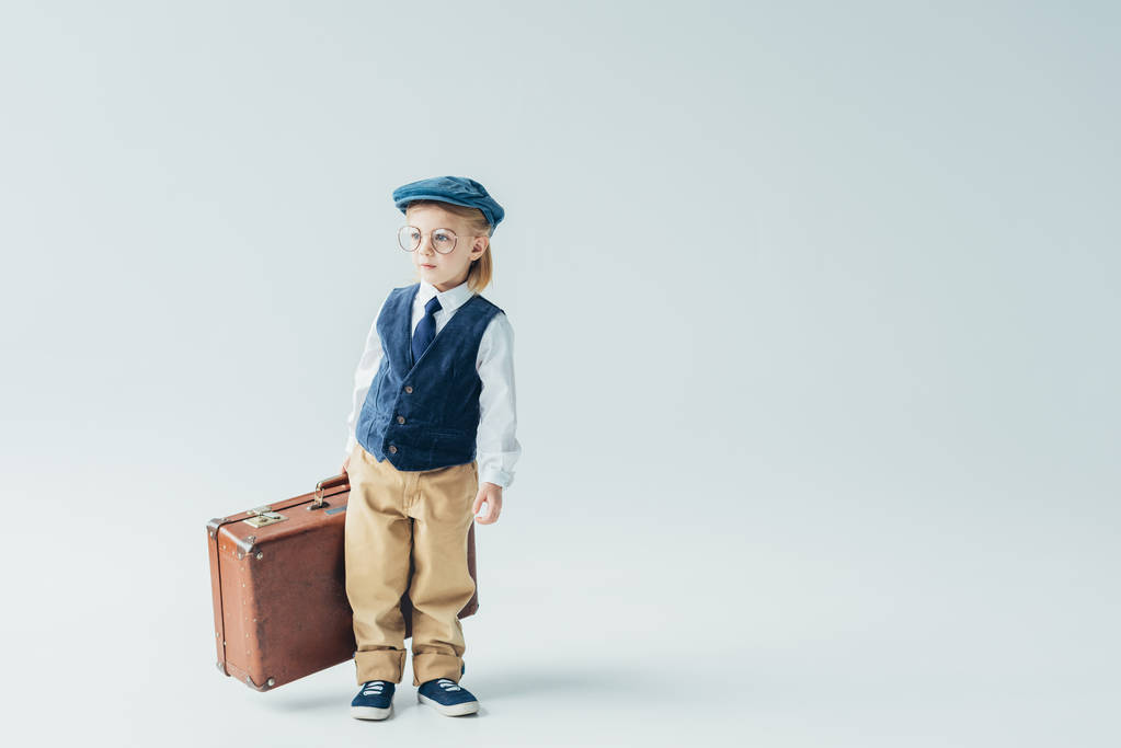  Kind in Retro-Weste und Mütze mit Koffer auf grauem Hintergrund  - Foto, Bild